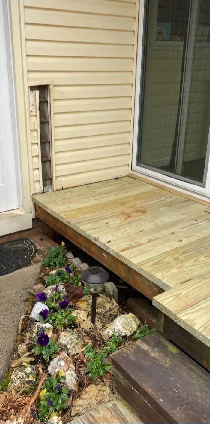 A new pressure treated wood landing built up to a sliding glass door in cream vinyl siding, a planted bed alongside