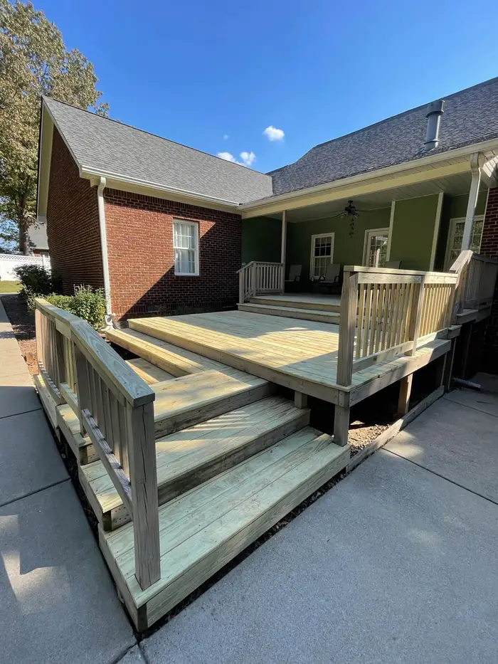 A wood deck with railings and open steps running down to a lawn, built against a brick house