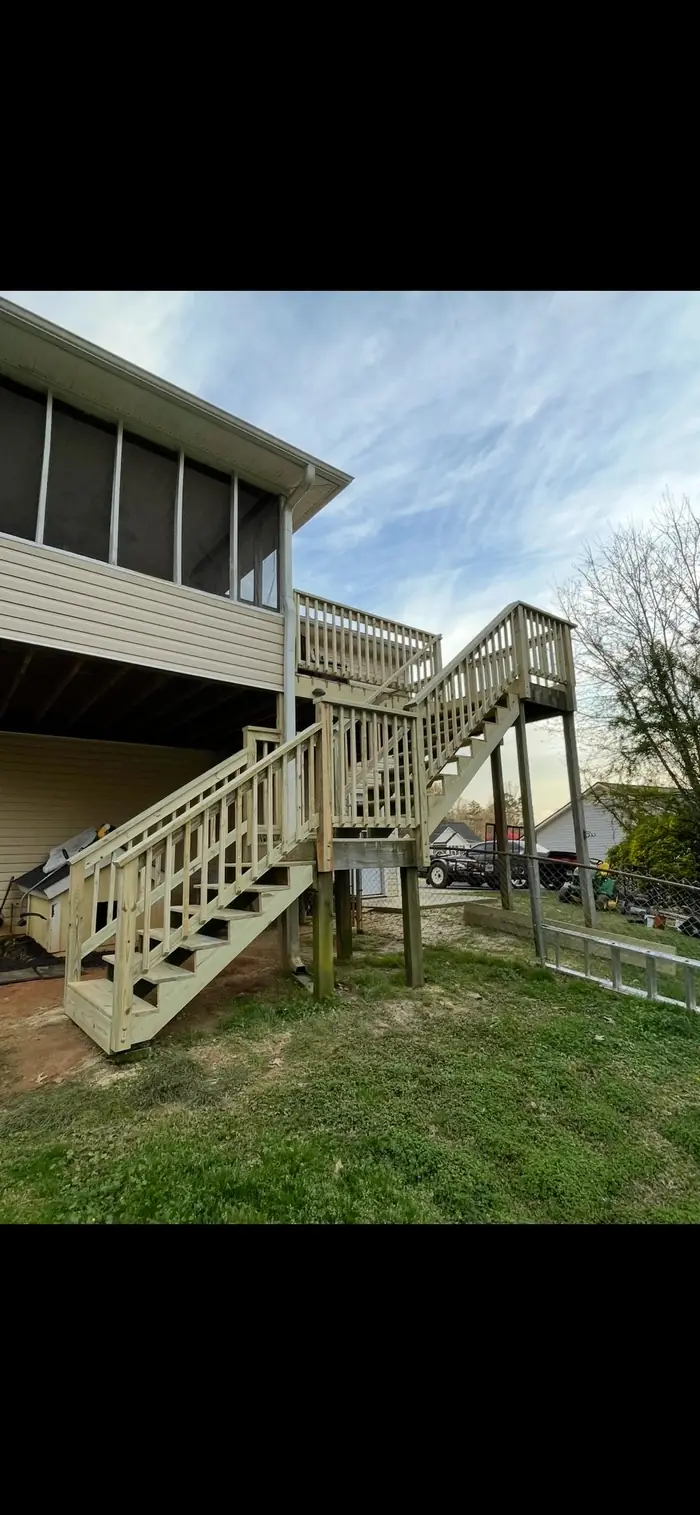 A raised deck with a long run of stairs and landings stepping down a sloped yard