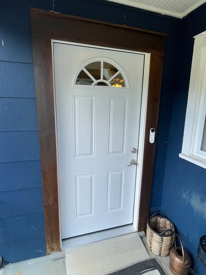 A white exterior door with a fan light, set in a dark wood frame in a wall of navy blue siding