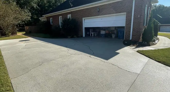 A concrete driveway washed back to clean gray in front of a brick house with an open garage