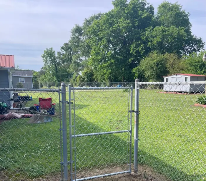 A run of chain link fence with a single walk gate latched shut, enclosing a level back yard
