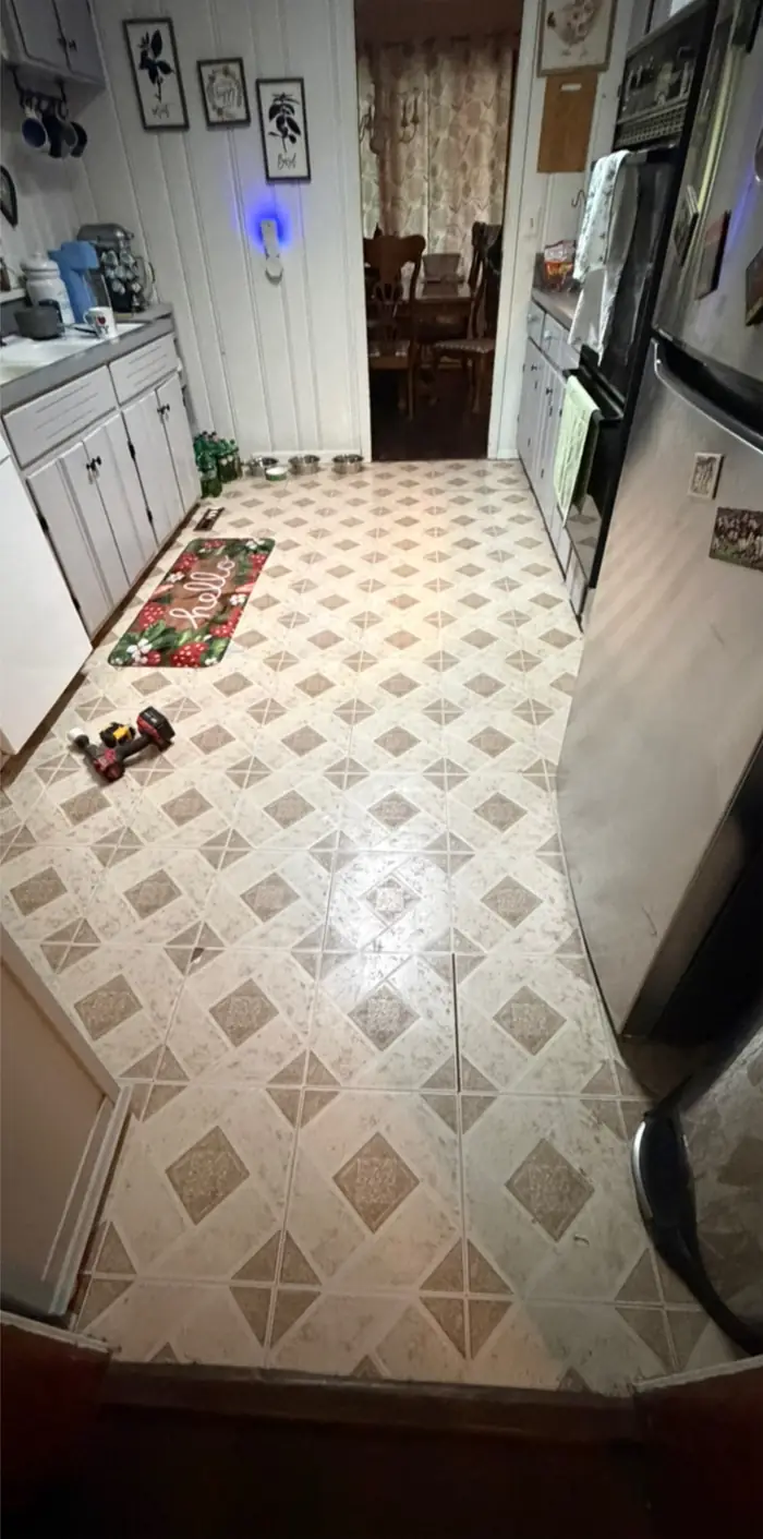 A kitchen floored in patterned sheet vinyl, running to the doorway of a dining room