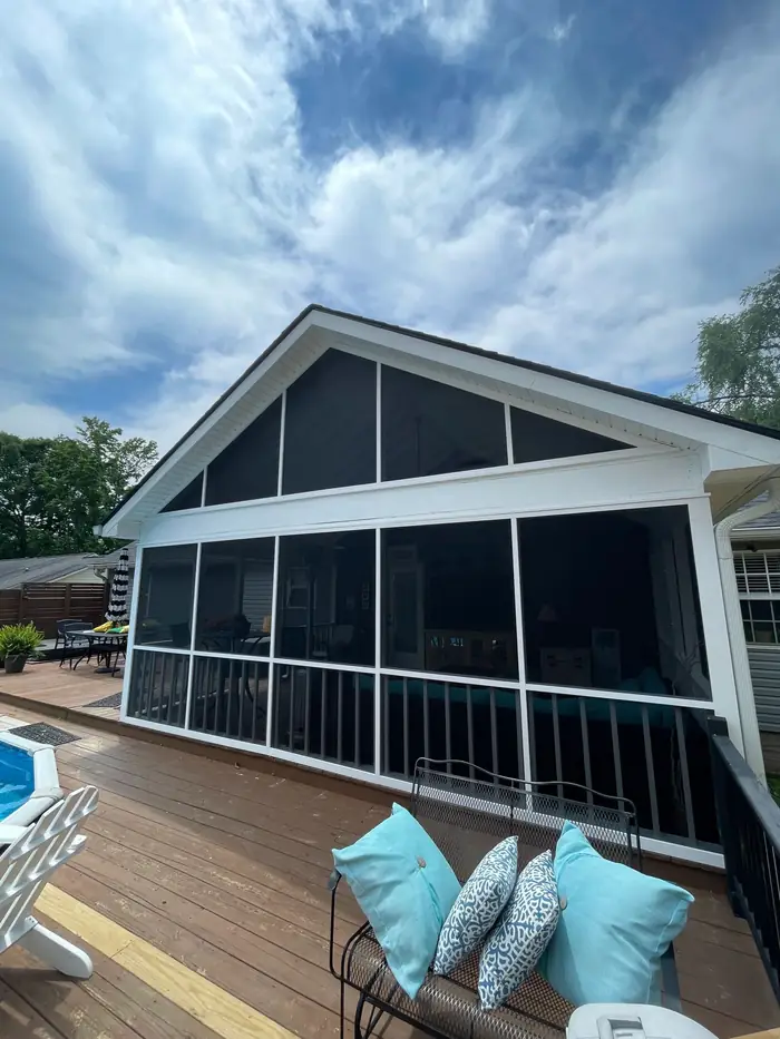 A finished screened porch beside a pool deck, with cushioned seating under the roof
