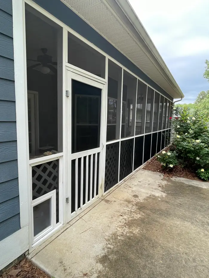 A long screened porch running down the side of a blue sided house, its panels framed in white, a concrete walk alongside