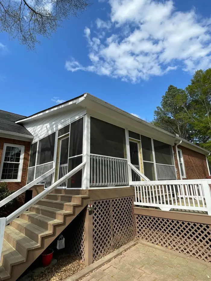 A screened porch with white railings and a flight of steps, lattice skirting below the deck