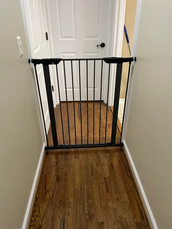 A safety gate fitted across a doorway at the top of a stairway, with refinished hardwood on the landing