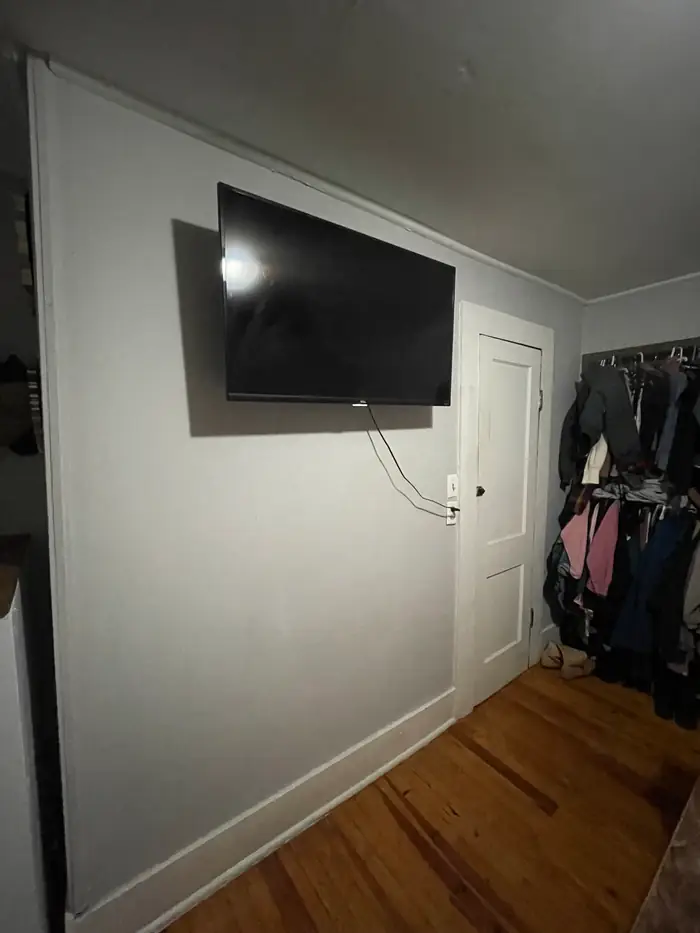 A flat screen television mounted flat against an interior wall, its cable dropped to the outlet below