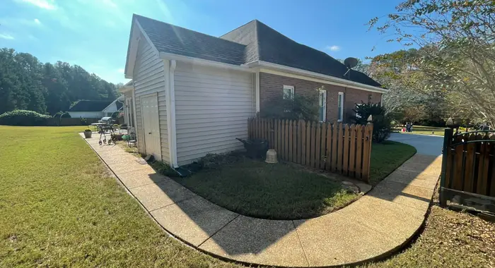 A concrete walk curving around the corner of a house to the driveway, past a wood privacy fence